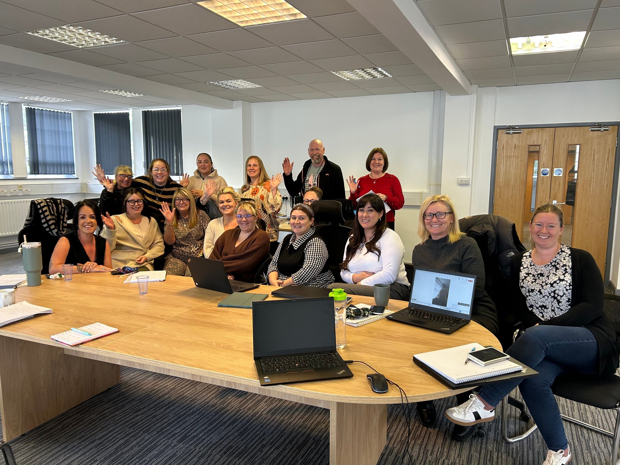 A group of Cartrefi colleagues in an office, waving at the camera